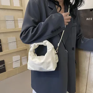 Detail of white pleated handbag with golden hardware and long leather shoulder strap