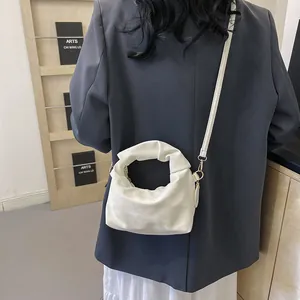 Close-up of white pleated cloud bag with shoulder strap shown on a gray blazer