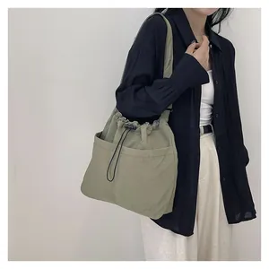 Sage green drawstring tote bag with dual front pockets shown in a styled casual outfit