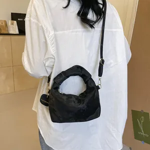 Close-up of black pleated handbag with gold hardware and a circular fashion tag charm