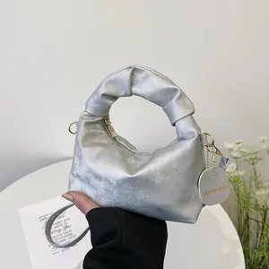 Detail of silver metallic handbag featuring a knotted handle and detachable shoulder strap