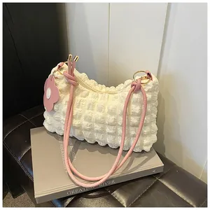 Detail of creamy white bubble textured shoulder bag with pink floral charm and strap