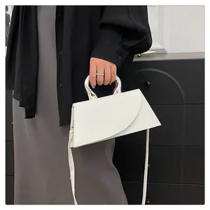 Detail einer minimalistischen creme-weißen Handtasche mit silbernem Metallgriff und Geometrie