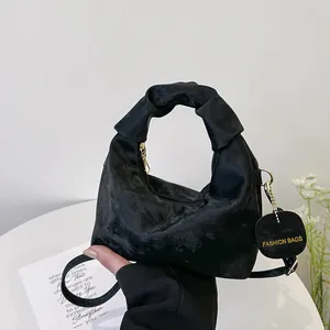 Detail of black velvet handbag with twisted handle and round brand tag in bright setting