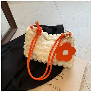 Detail of white pleated handbag with orange tubular strap and floral bag charm