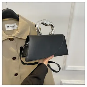 Detail einer schwarzen Trapez-Handtasche mit silbernem Metallgriff und Schultergurt