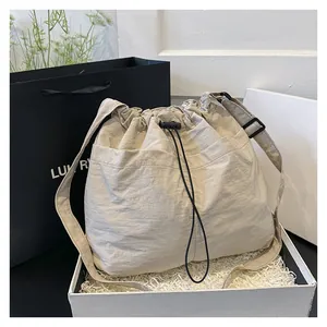 Detail of beige drawstring bag with textured nylon fabric and side pockets in a gift box