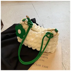 Detail of cream white bubble textured bag with vibrant green knotted straps and flower charm