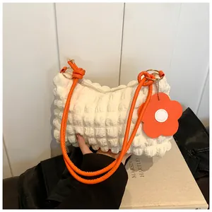 Detail of white pleated bubble fabric bag with orange knotted strap and daisy charm
