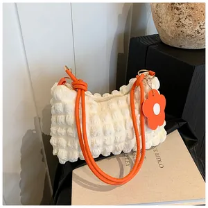Detail of white textured ruched fabric bag with bright orange handle and flower charm