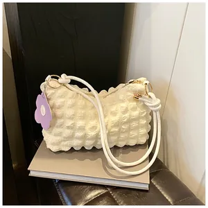 Detail of white pleated bag with bubble texture, rope strap and purple flower charm