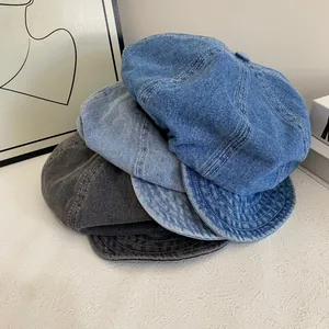 Detail of washed denim newsboy caps in navy, light blue, and grey on a white surface
