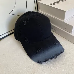 Vintage black distressed baseball cap with ripped details on a white textured surface