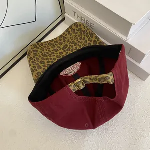 Detail view of burgundy baseball cap with leopard print brim and adjustable metal buckle