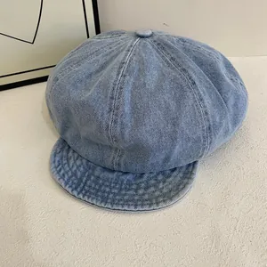Close-up of light blue denim newsboy hat with top button on textured white background