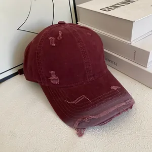 Detailed macro view of distressed holes and raw edges on a vintage burgundy baseball cap