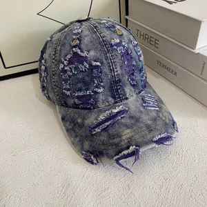 Close-up of distressed denim baseball cap with purple fabric lining peeking through ripped holes
