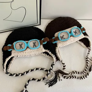 Detail of knitted aviator beanies in black and brown with goggle decor and tassels