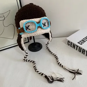 Detail of crochet pilot knit hat with goggles decor and long braided tassels