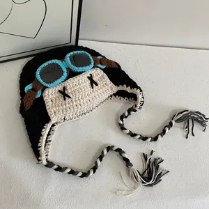 Detail view of a crocheted aviator beanies with goggles design and tassels