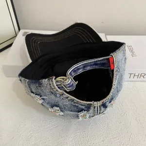 Detail of distressed denim baseball cap featuring metal buckle and red woven label