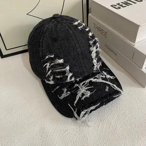 Detailed view of the distressed black denim baseball cap with heavy frayed hole accents