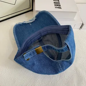 Detail view of denim baseball cap with frayed edges and adjustable metal buckle strap