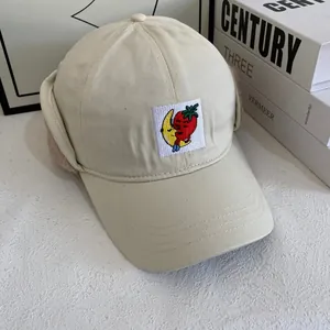 Close-up of beige winter baseball cap featuring plush ear flaps and strawberry embroidery