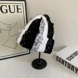 Detail of chunky knit black and white striped beanie on a minimalist stand