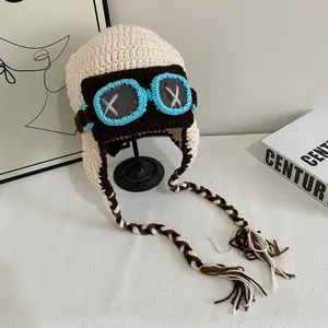 Chic cream knit pilot aviator hat with goggles and braided tassels on a stand