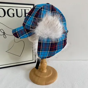 Chapeau trappeur à carreaux bleus avec pompons en fausse fourrure sur support en bois
