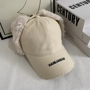 Detail of beige aviator hat with faux rabbit fur ear flaps and black letter embroidery