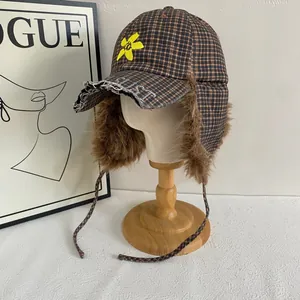 Detail of checkered earflap hat with brown faux fur lining and yellow flower embroidery