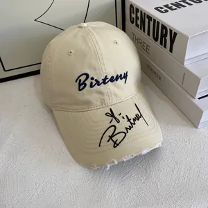 Close-up of beige baseball cap featuring Birteny embroidery and distressed brim details
