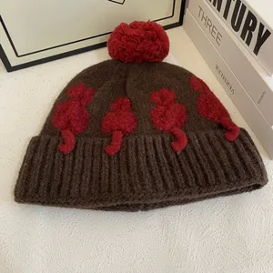 Texture a maglia del berretto marrone con motivo a gatto e pompon rosso grande