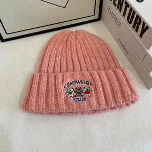 Detalle del gorro de punto rosa con bordado de tres ositos y textura de lana suave