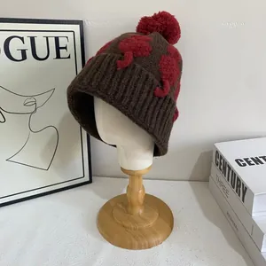Dettaglio del cappello in maglia marrone con motivi di elefanti rossi e grande pompon