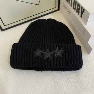 Detalle del gorro de punto acanalado negro con tres parches de estrellas de cuero en el dobladillo