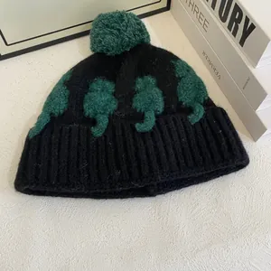 Dettaglio del berretto in maglia nera con pompon verde e motivi a sagoma di gatto