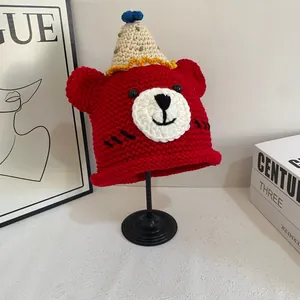 Detail of red handmade crochet bear hat with a beige party hat topper on a metal stand