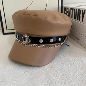 Detailed close-up of brown faux leather newsboy cap with anchor charm and chain detail