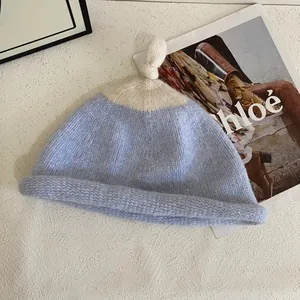 Detail of baby knitted pacifier hat featuring light blue contrast and top knot decoration