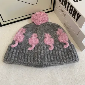 Dettaglio del berretto in maglia grigia con pompon rosa e motivi a gatto 3D all'uncinetto