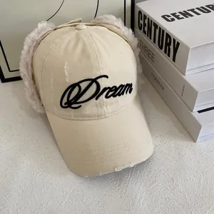 Détail d'une casquette en toile beige avec protège-oreilles en peluche et broderie Dream