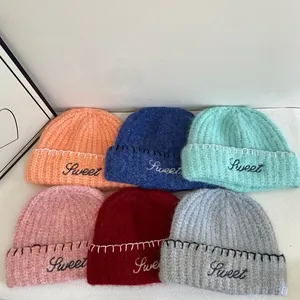 Close-up of thick knit beanies with Sweet embroidery and contrast stitching details