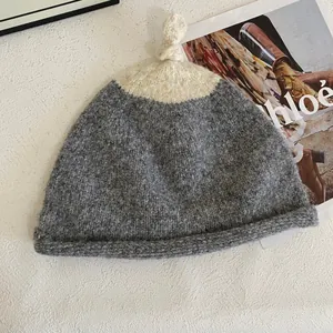 Detail of two-tone knit beanie featuring thick grey and cream texture and top knot