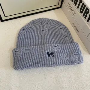 Detail of light blue knit beanie featuring distressed holes and dark blue dog embroidery