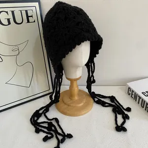 Détail du bonnet au crochet noir fait main avec fleurs tricotées et longs pompons de style