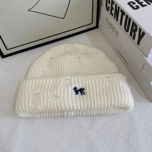 Detail of cream rib-knit beanie with distressed hole design and blue dog embroidery
