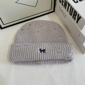 Detailed close-up of light gray ribbed knit beanie with blue dog embroidery and distressed holes